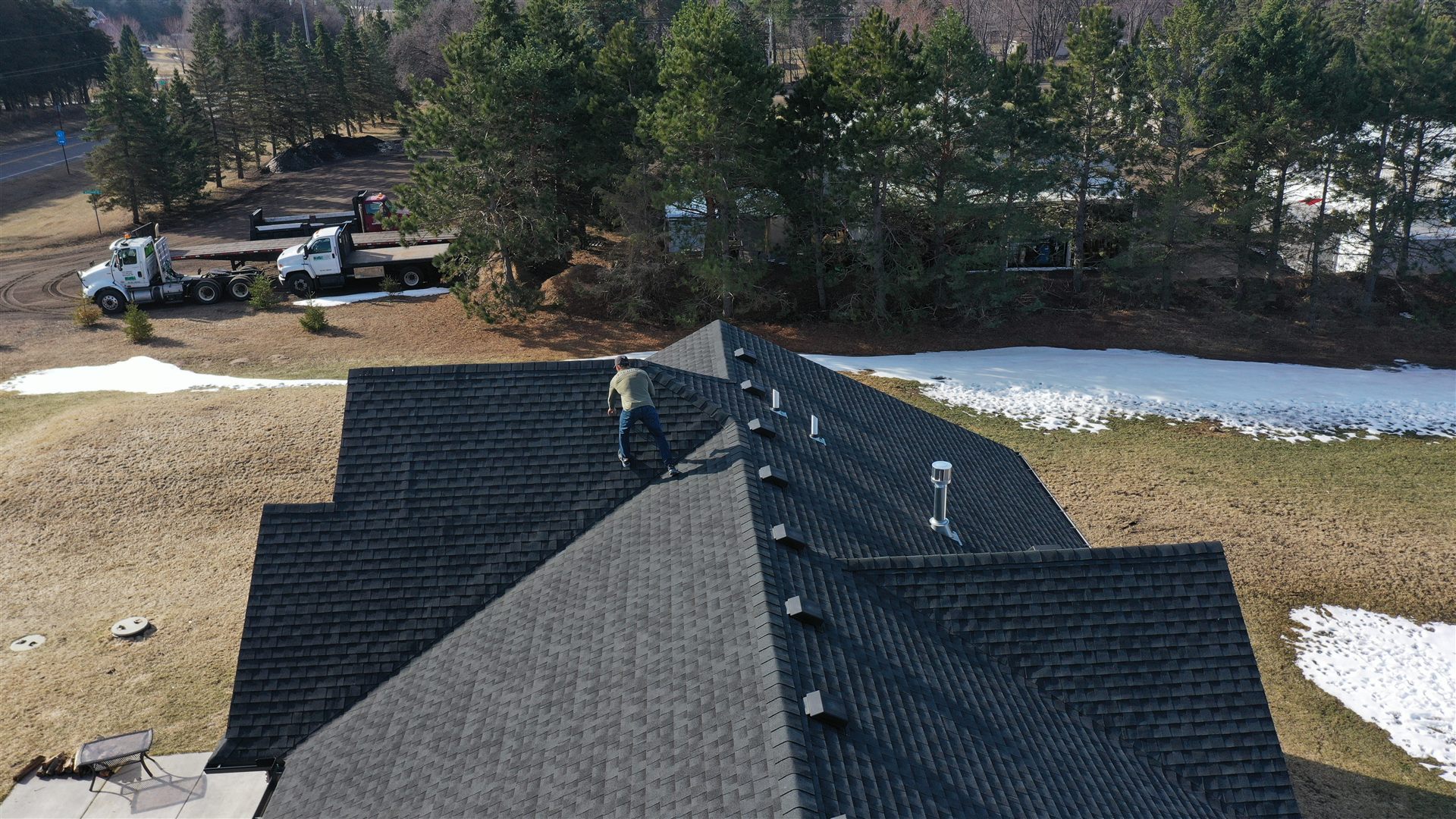 Aerial view of Tom Jacobs inspecting a completed roof replacement with delivery trucks below