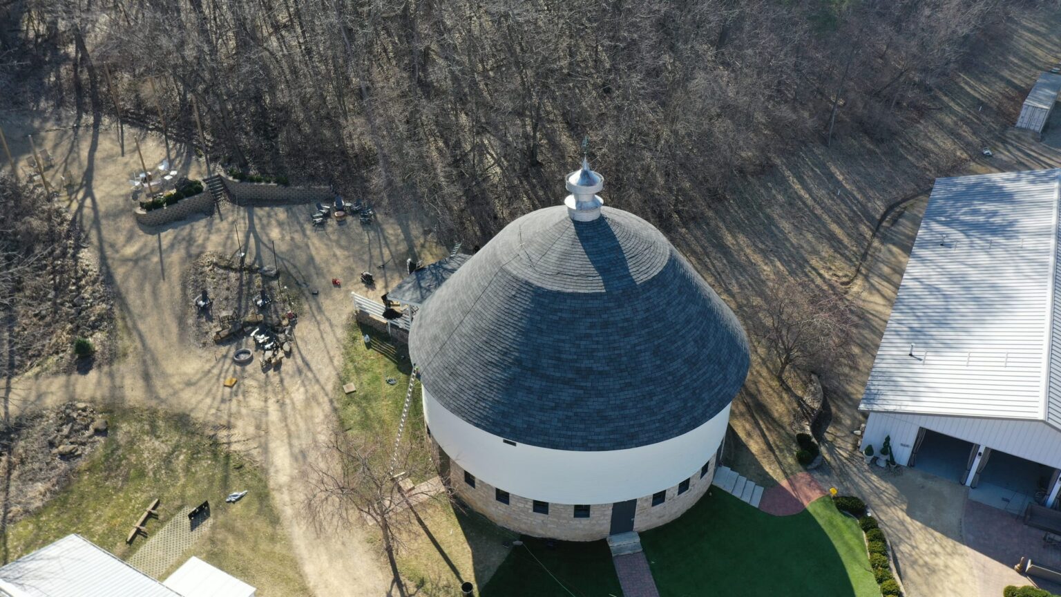 Crew member installing shingles on the round barn roof, radial courses visible