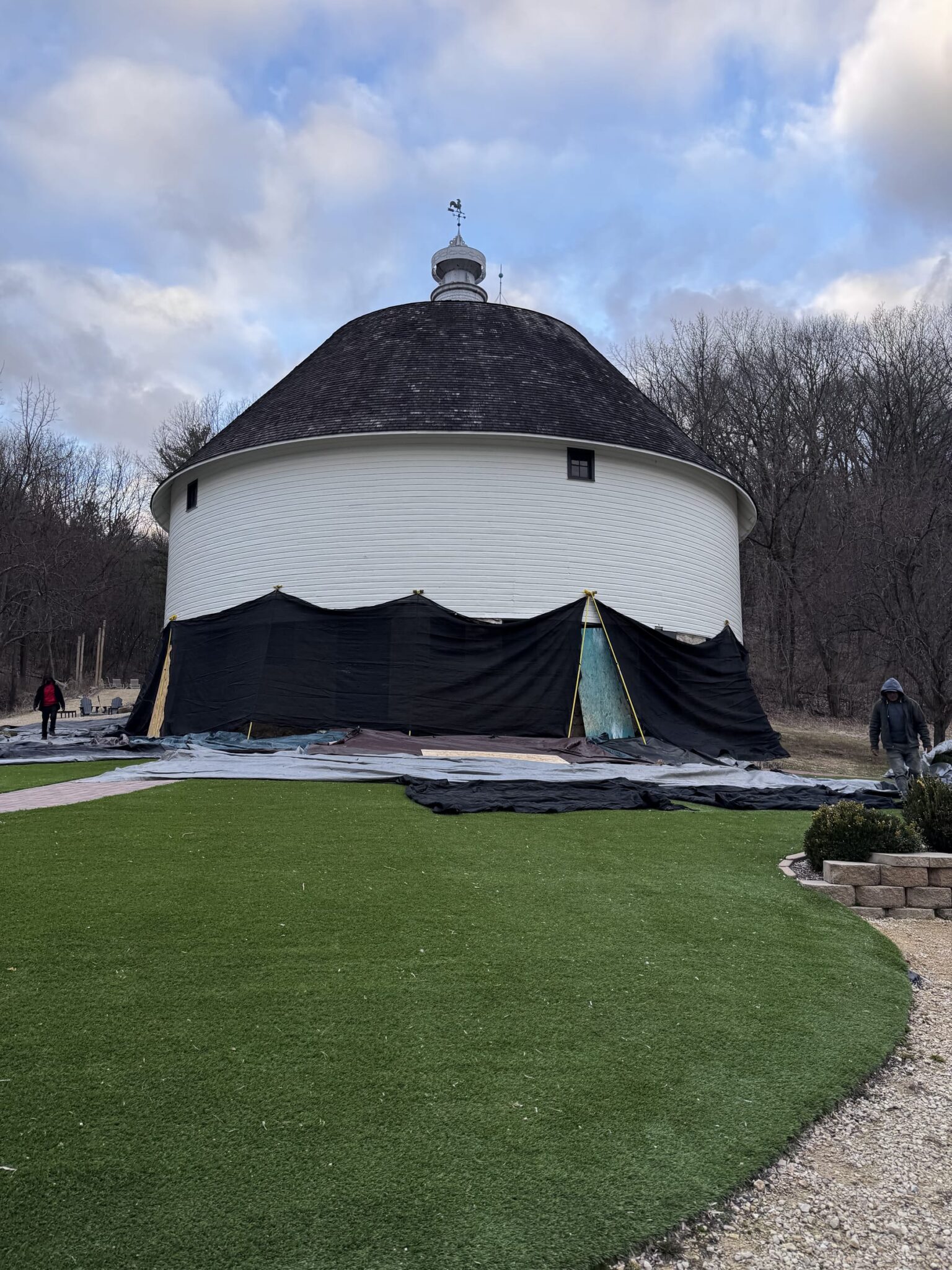 Protective tarping wrapped around the round barn's base before roof tear-off