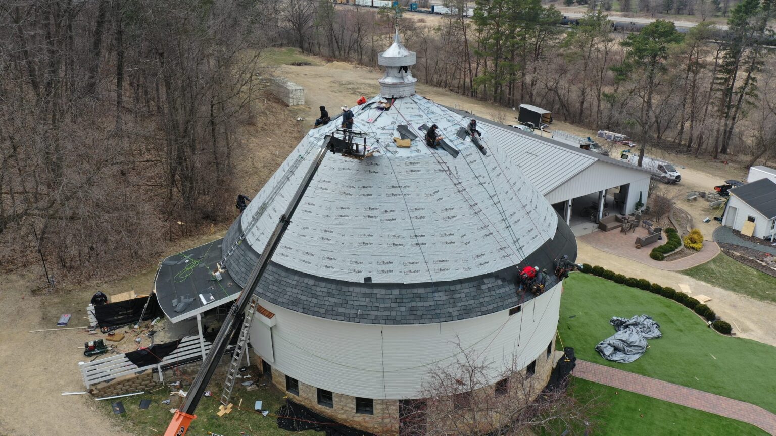 Jacobs Construction crew member shingling the round barn dome, aerial view